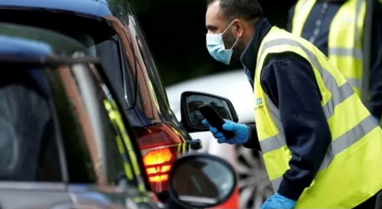 A member of staff wearing a mask, approaching a car window at a testing centre