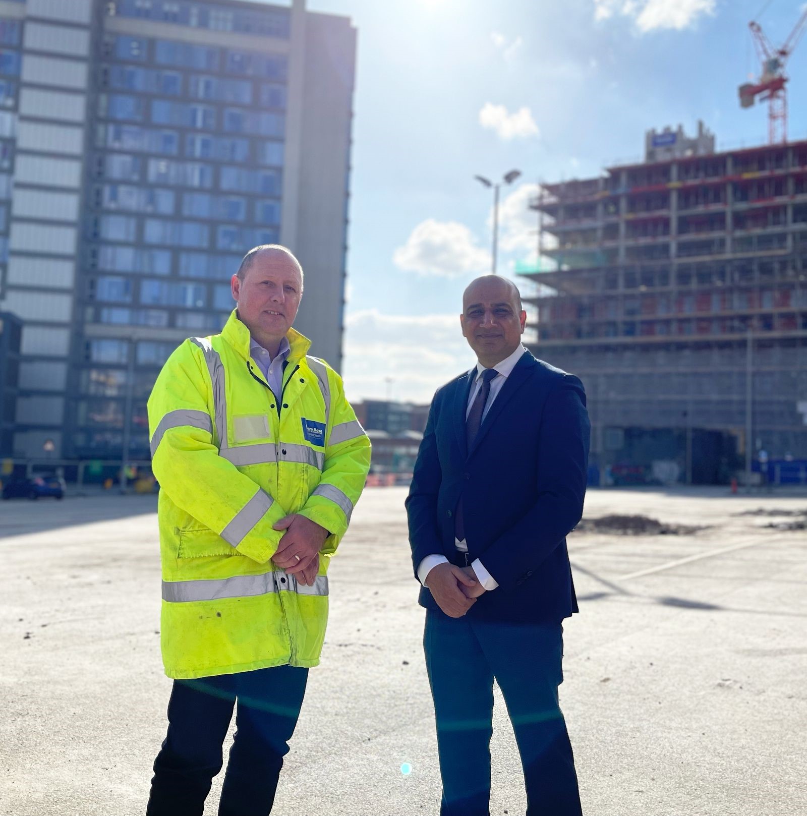 Two men stood on construction site, one in high vis, one in a suit. 
