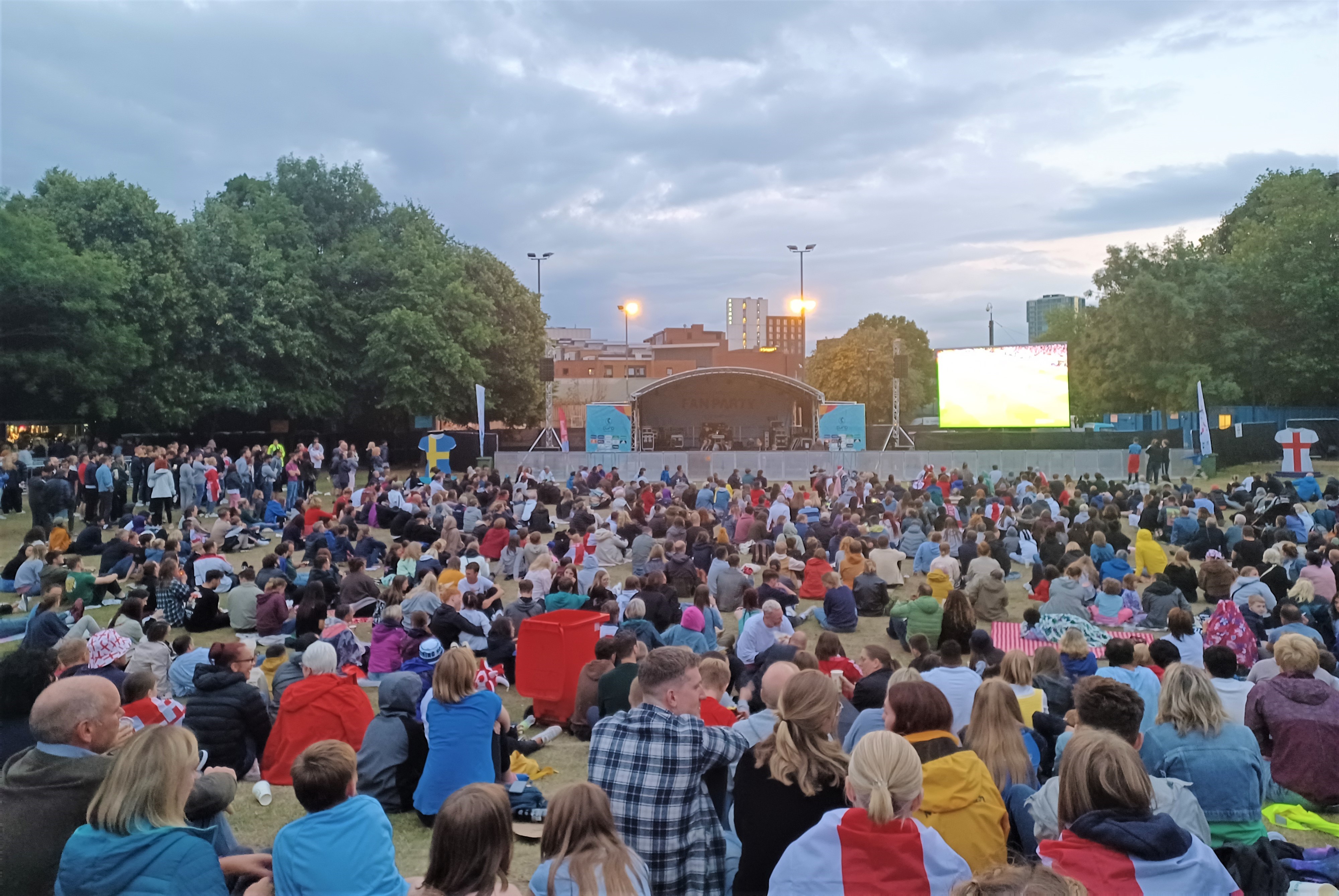 A crowd of people sitting in front of a large stage and screen on Devonshire Green in Sheffield
