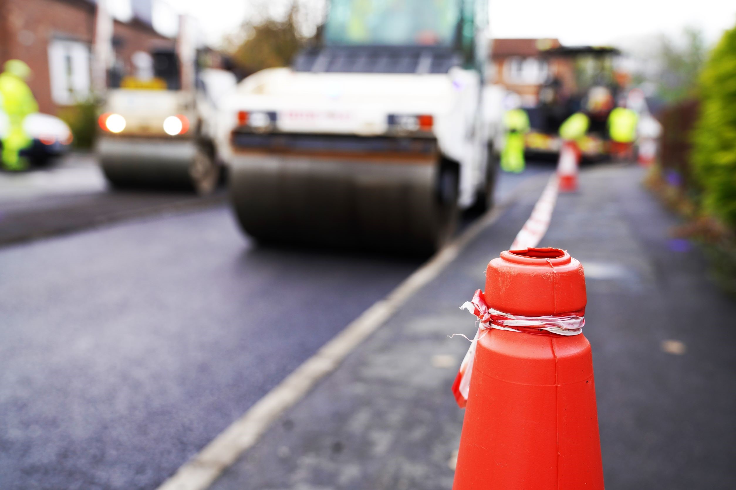 An orange cone in front of a blurred tarmac roller