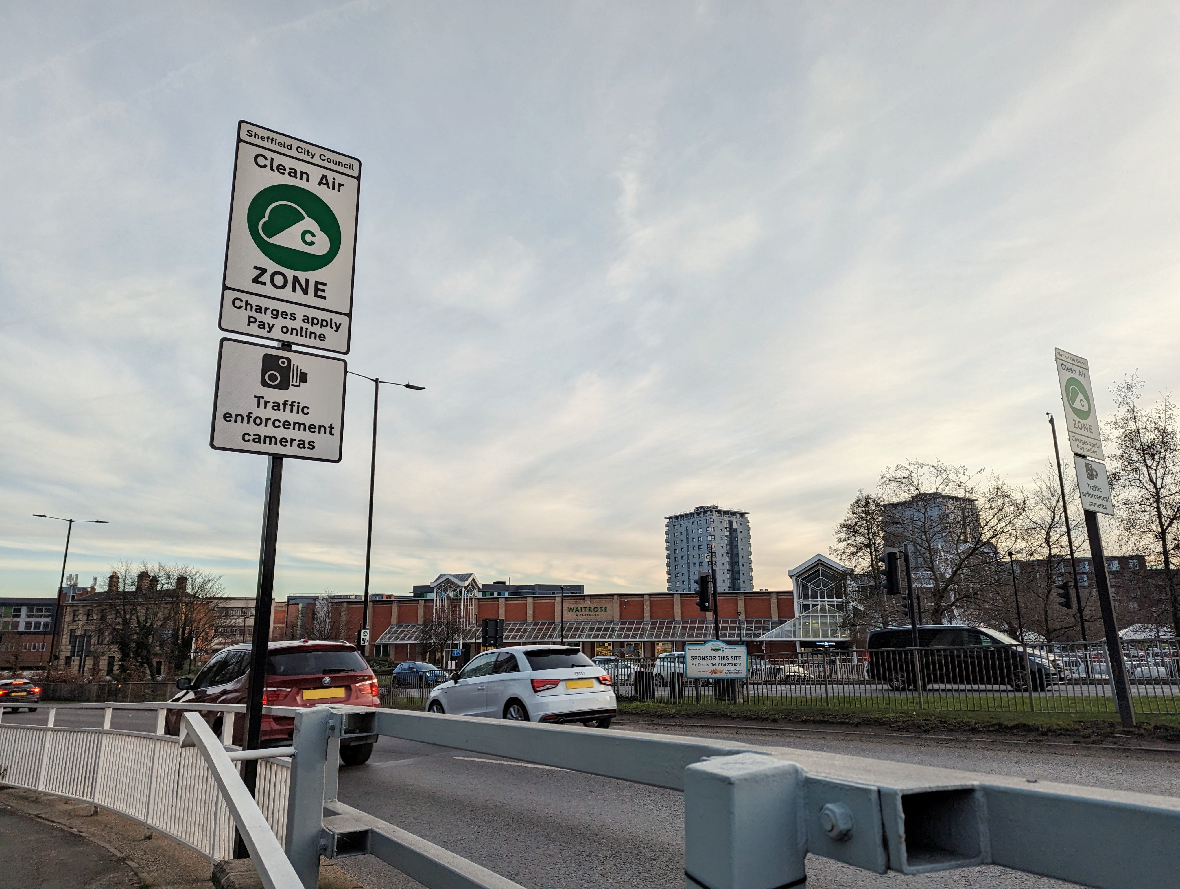 A white road sign informs drivers on the side of the road that they could be liable for a Clean Air Zone charge if their vehicle is not compliant. 