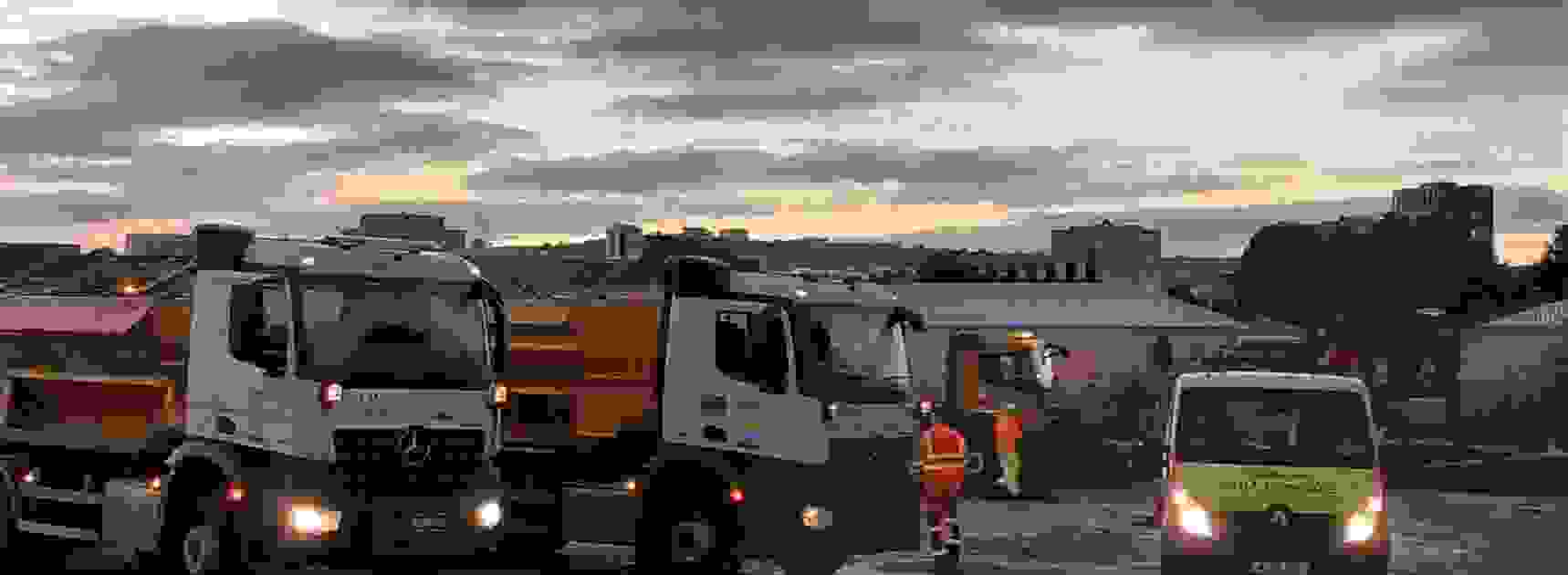 Two gritter lorries at dusk at works depot with pink and blue dusk sky