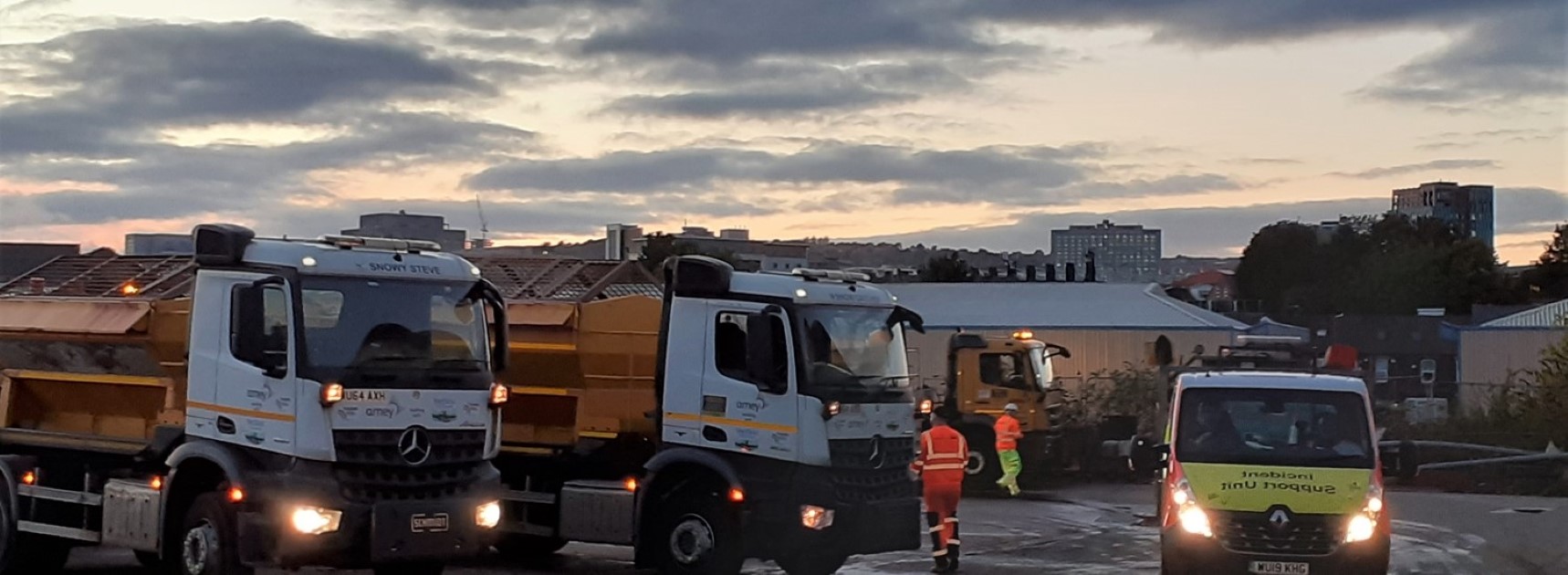 Two gritter lorries at dusk at works depot with pink and blue dusk sky