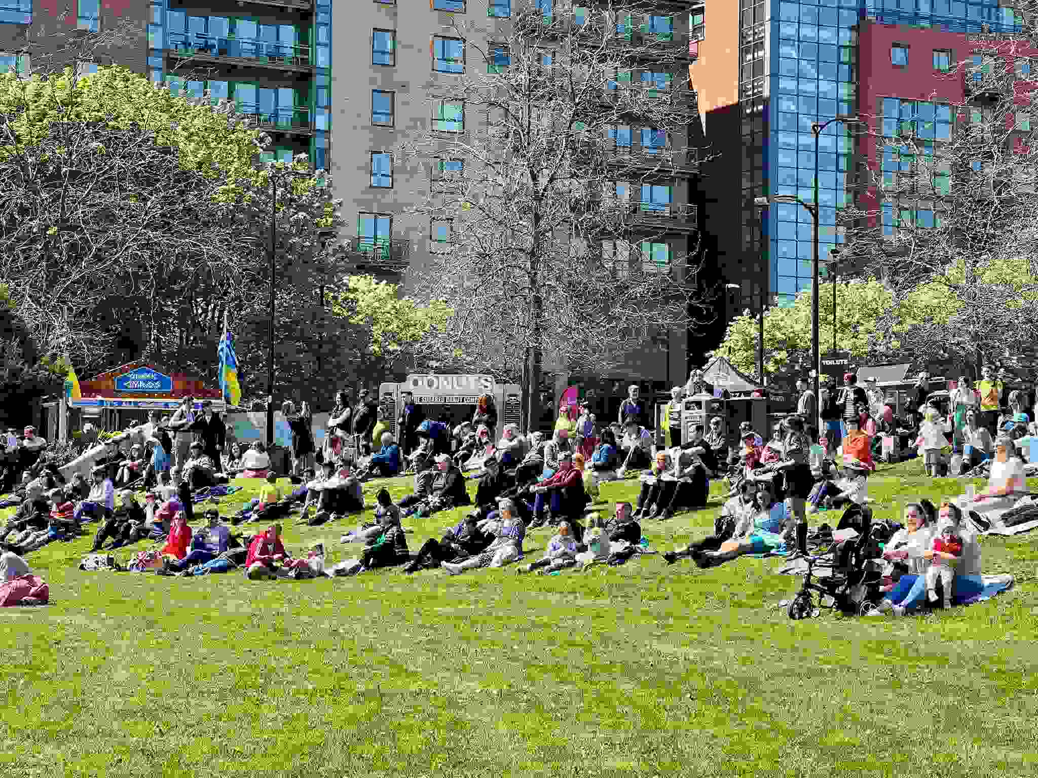 People sit on Sheffield's Devonshire Green in the sunshine, watching acts perform on stage