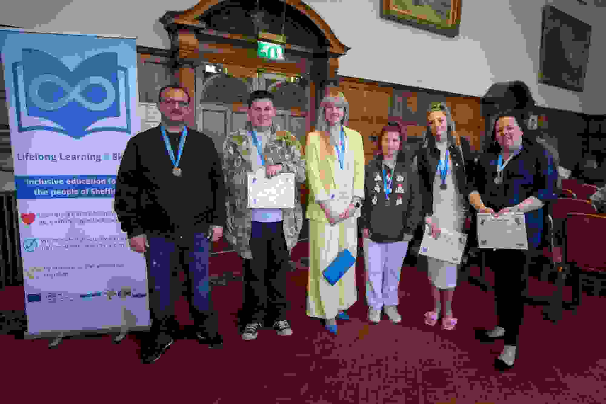 Six people stand in a line in front of a banner for Lifelong Learning in Sheffield Town Hall. 