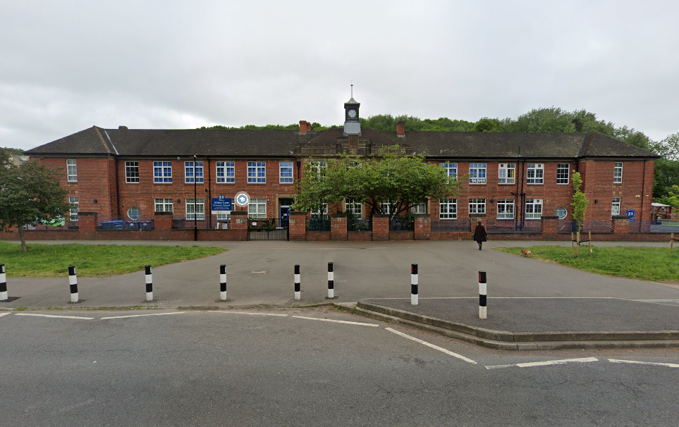 red brick school building with white- framed windows, grass and black and white road bollards in the foreground
