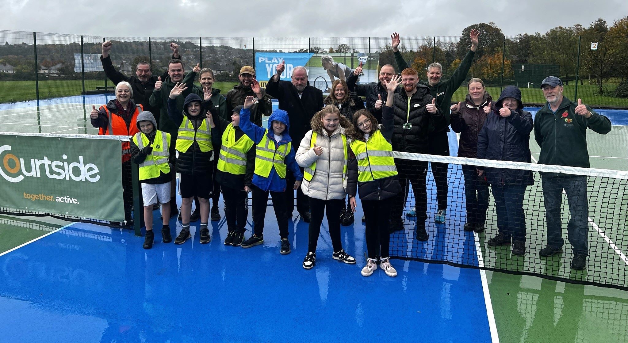 Schoolchildren in front row on tennis court in yellow hi-vis with SCC officers, Councillor Richard Williams, Friends of Hollinsend Park and LTA officers 