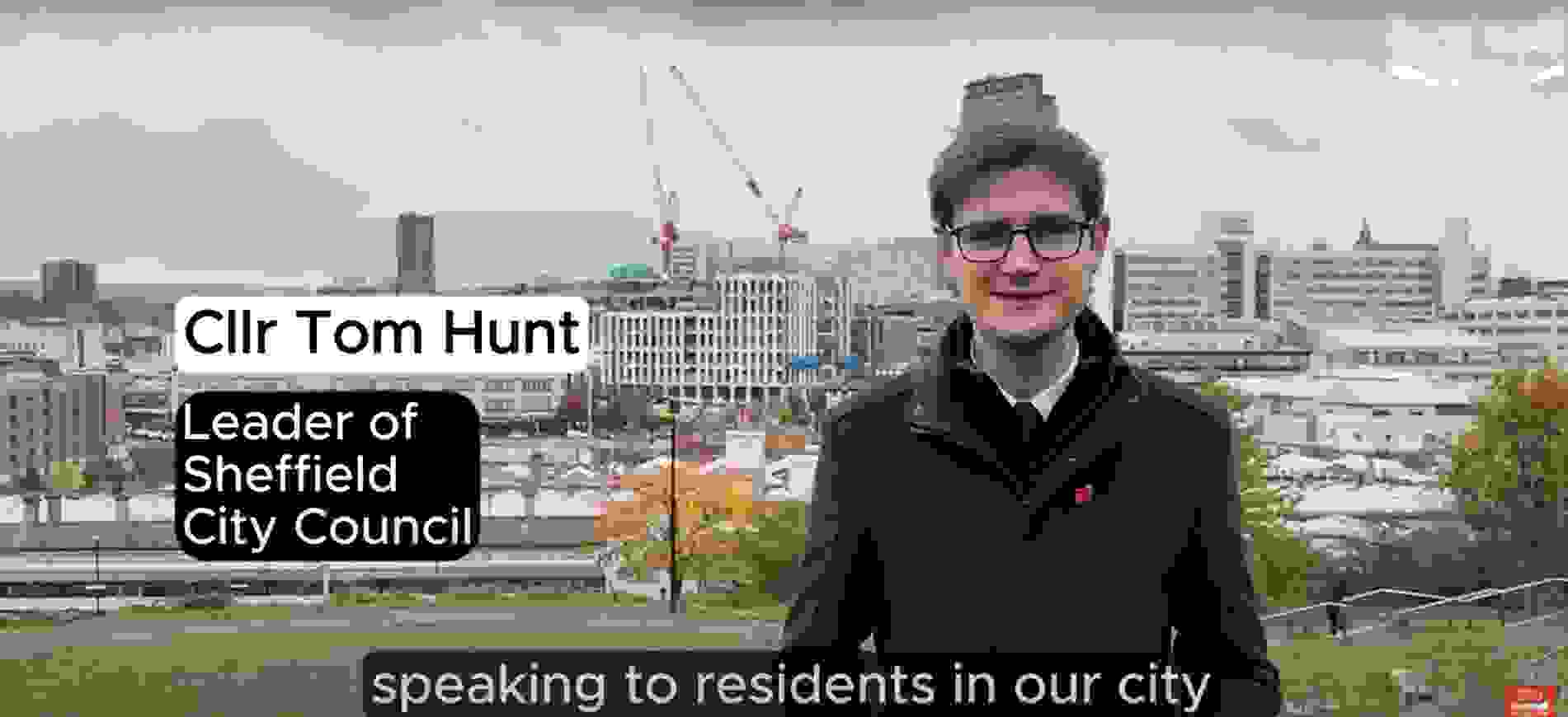 Councillor Tom Hunt, stood infront of a Sheffield skyline, showing cranes and buildings. Tom is wearing a dark coat with a red poppy badge for Remembrance Sunday.  