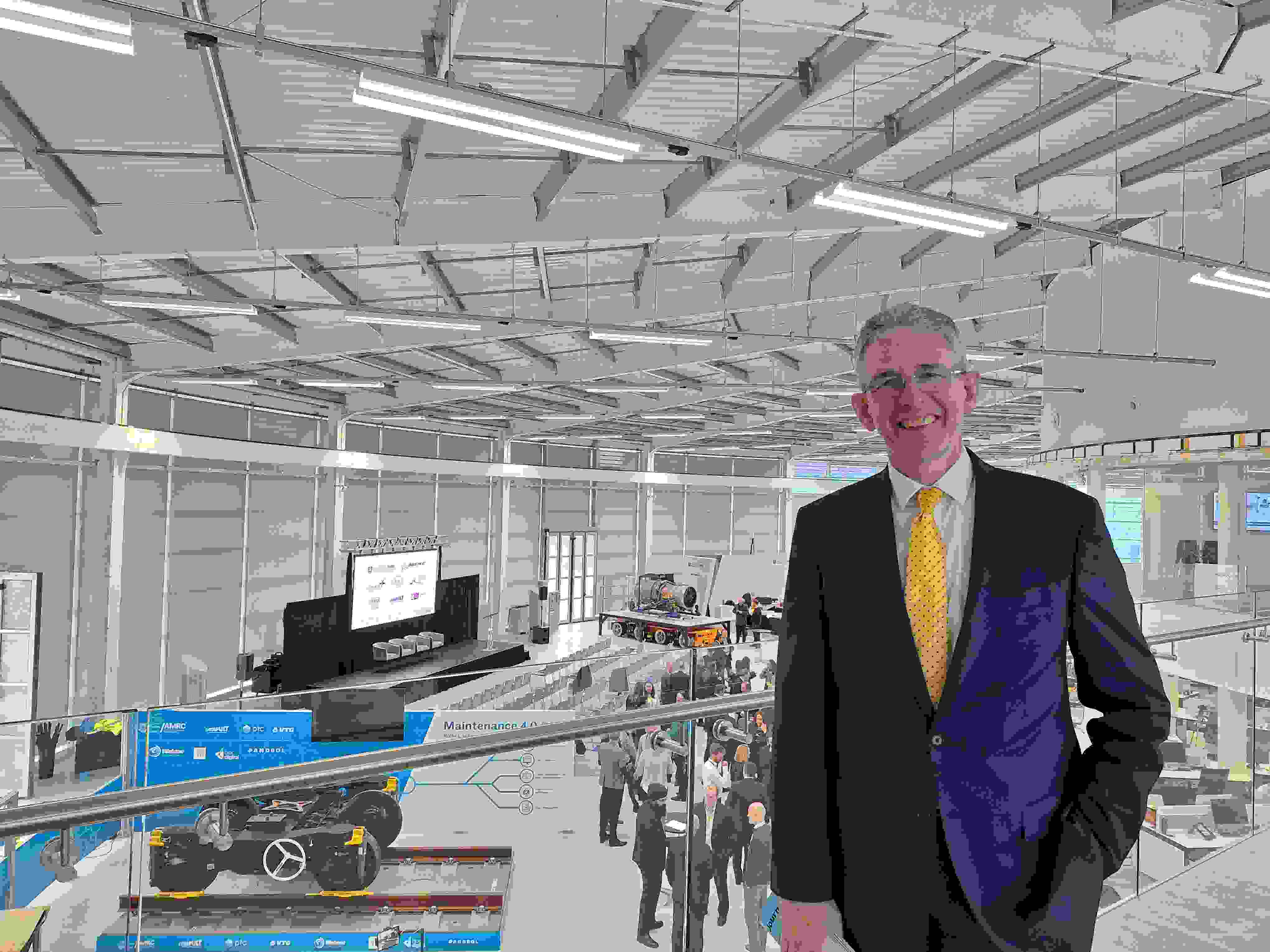 Councillor Martin Smith, stood inside the AMRC at the University of Sheffield, behind him are people enjoying the groundbreaking event which shows  a robot resembling a vehicle