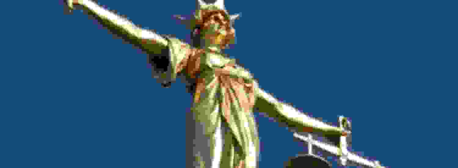 A statue of the Scales of Justice in front of a clear blue sky