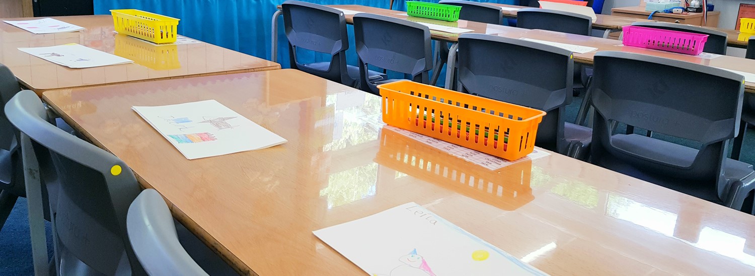 a school classroom with papers on the table, including an orange storage box