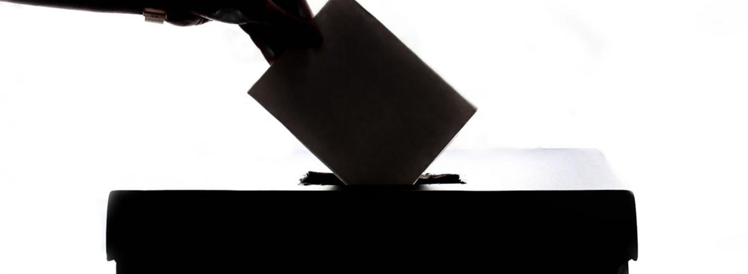A hand putting a voting ballot into a ballot box