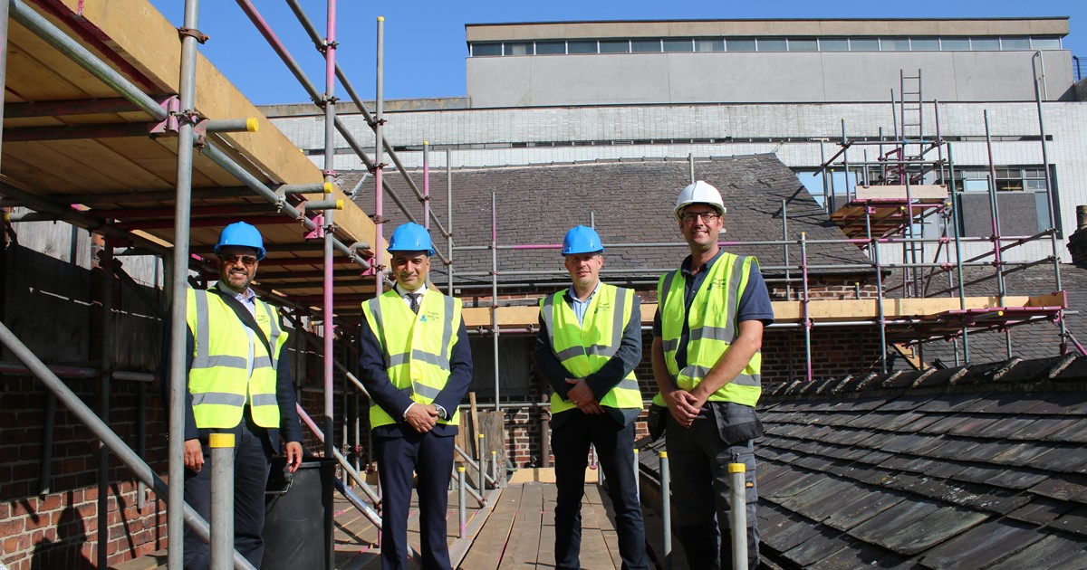 Four men stood on a roof top in highly visible clothing.