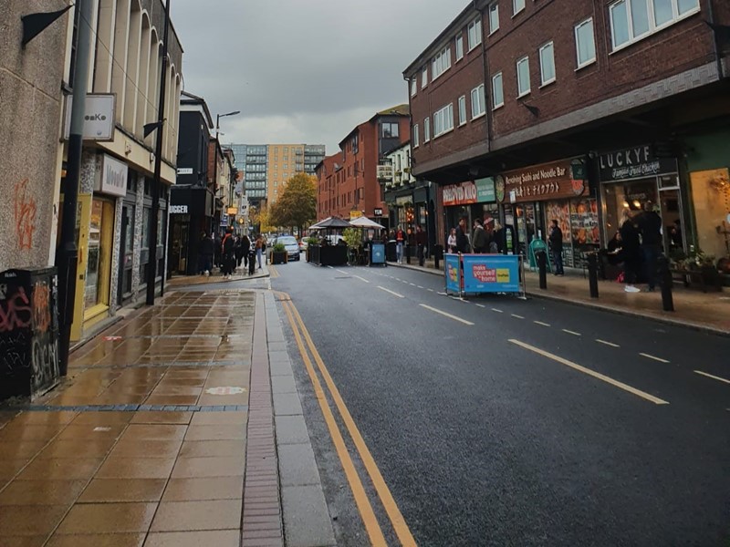 Road and pavement surrounded by buildings and a grey sky