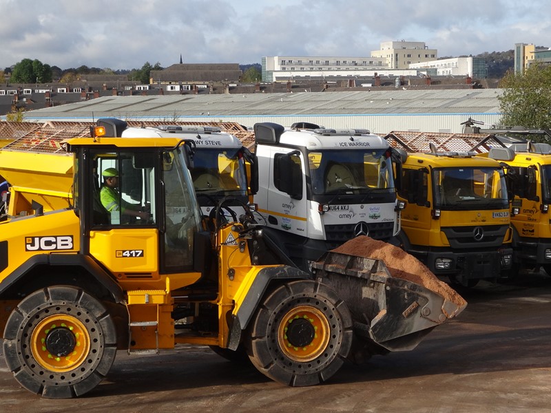 Yellow tractor in front of gritting lorries.