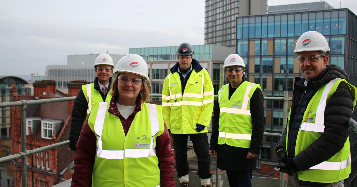 Five people in hi-vis and hard hats stood on top of a building