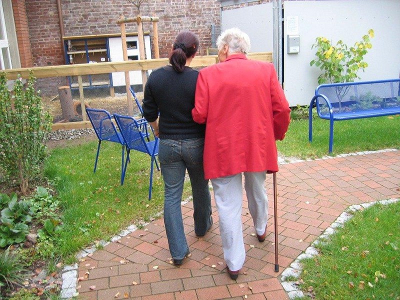 Older lady with stick walking with carer/support