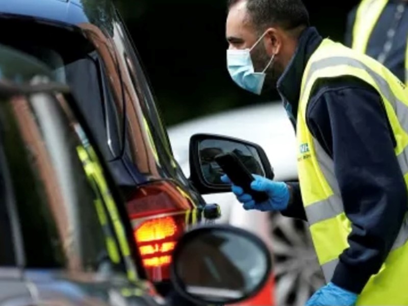 A member of staff wearing a mask, approaching a car window at a testing centre