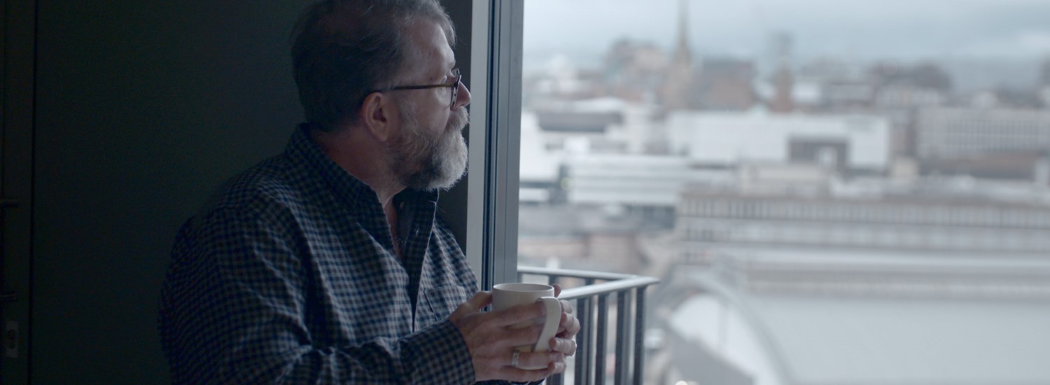 Man holding a cup looking out of a window