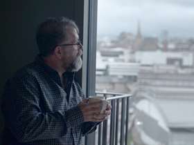 Man holding a cup looking out of a window