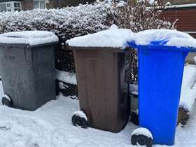 A black, blue and brown bin on snowy ground, and with snow on the lids