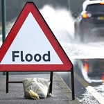 Flooding updates - October 2023 Image of a flood warning sign, in a red triangle on a road where cars are driving through water.