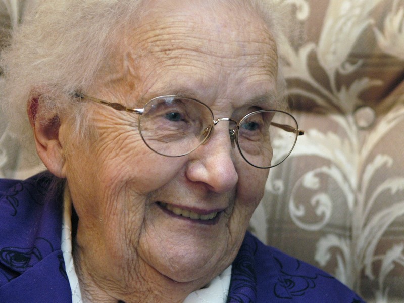 Older woman at home on sofa in blue jacket and white shirt