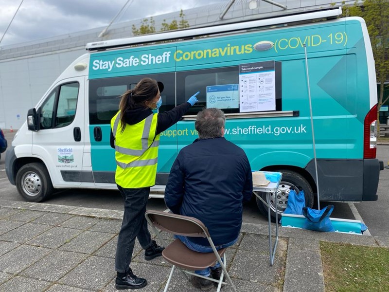 Blue/green and white large van with man sitting outside and staff member pointing at van