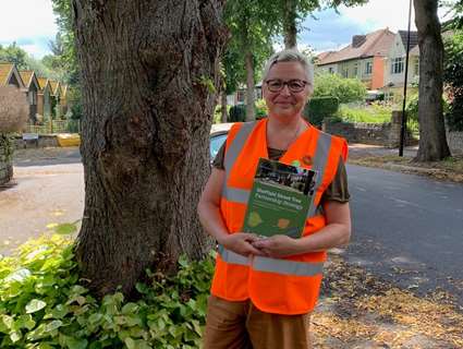 Woman in high vis jacket stands in front of tree on street