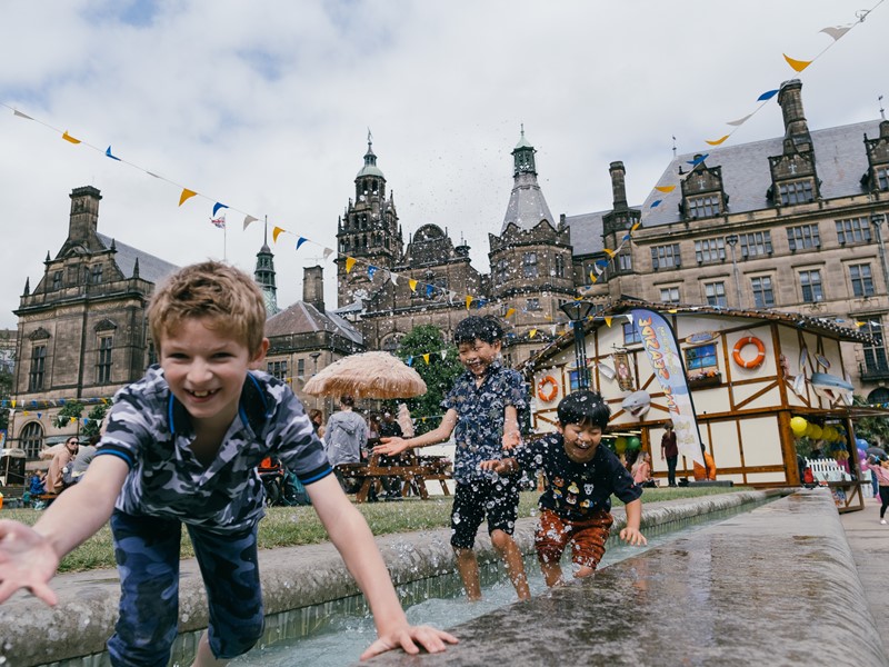Three young children play in the fountains outside Sheffield Town Hall