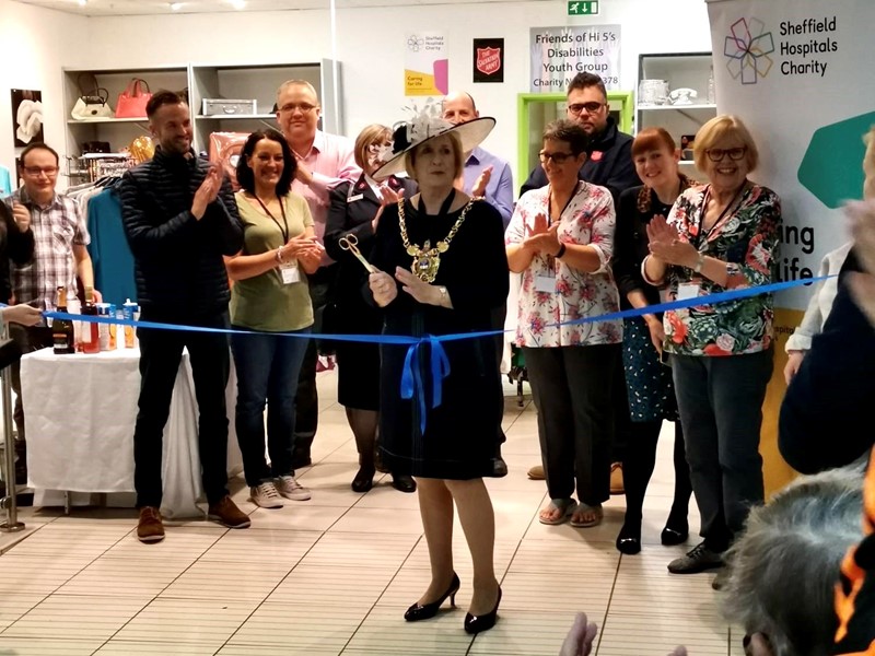 Lord Mayor Gail Smith holds a pair of scissors to cut a blue ribbon declaring her new charity shop in Crystal Peaks open to the public and joined by a group of applauding onlookers