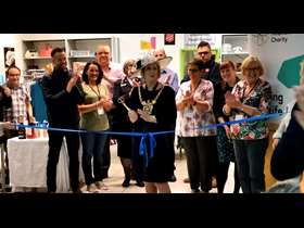 Lord Mayor Gail Smith holds a pair of scissors to cut a blue ribbon declaring her new charity shop in Crystal Peaks open to the public and joined by a group of applauding onlookers