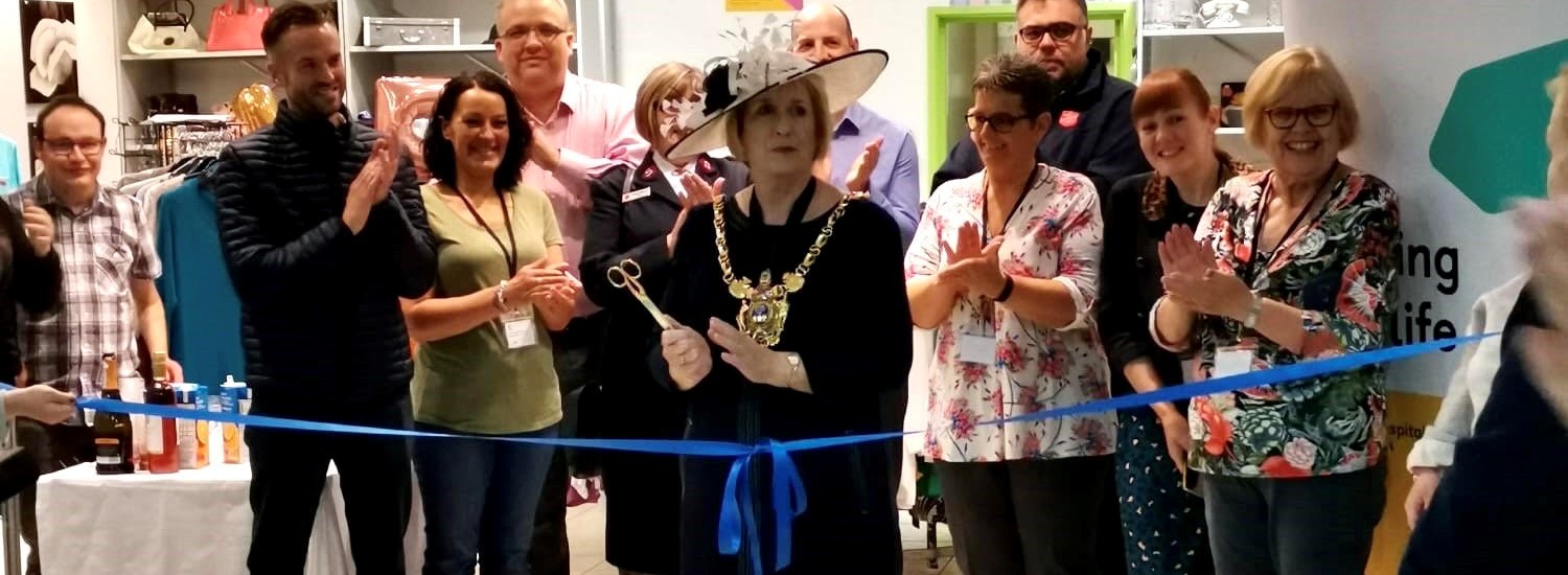 Lord Mayor Gail Smith holds a pair of scissors to cut a blue ribbon declaring her new charity shop in Crystal Peaks open to the public and joined by a group of applauding onlookers