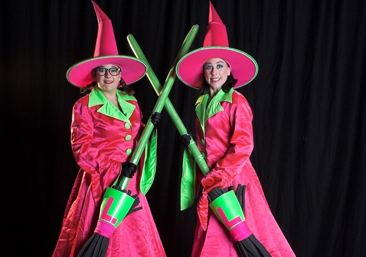 Pink Witches promotional image pose with their green broomsticks