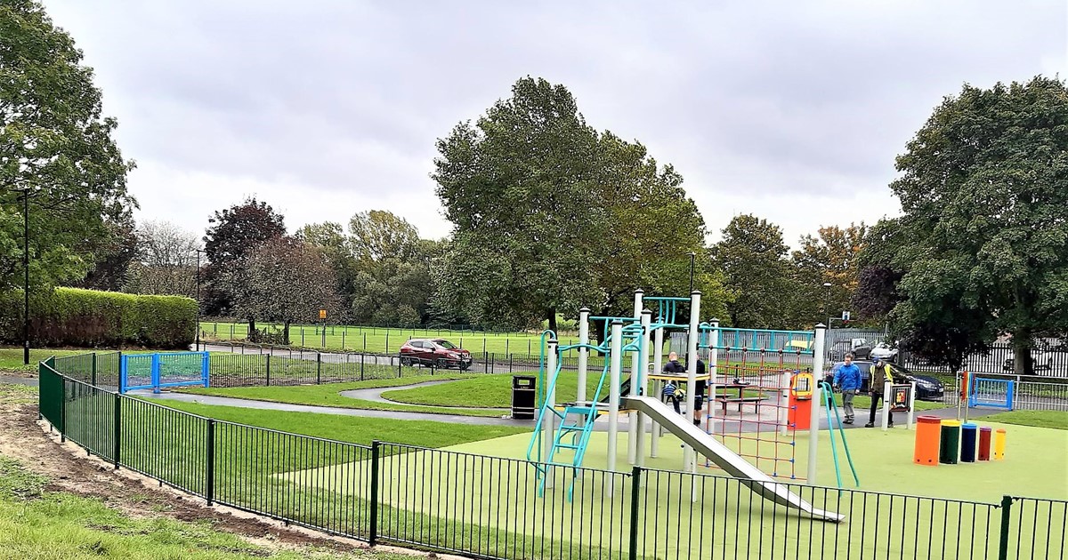 Play equipment with fenced enclosure set amongst green space and trees