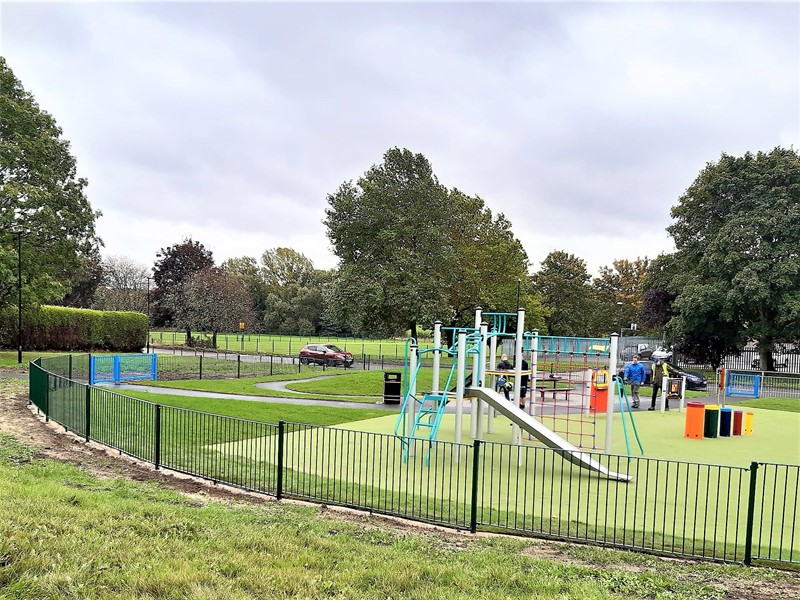 Play equipment with fenced enclosure set amongst green space and trees