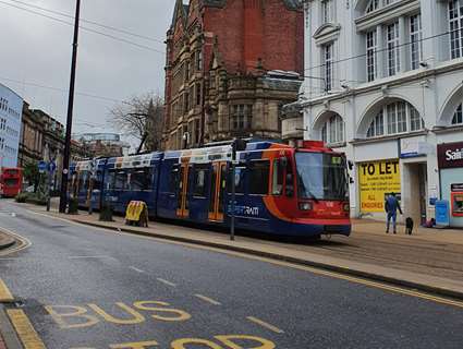 A red, blue and orange Supertram drives through Sheffield City Centre