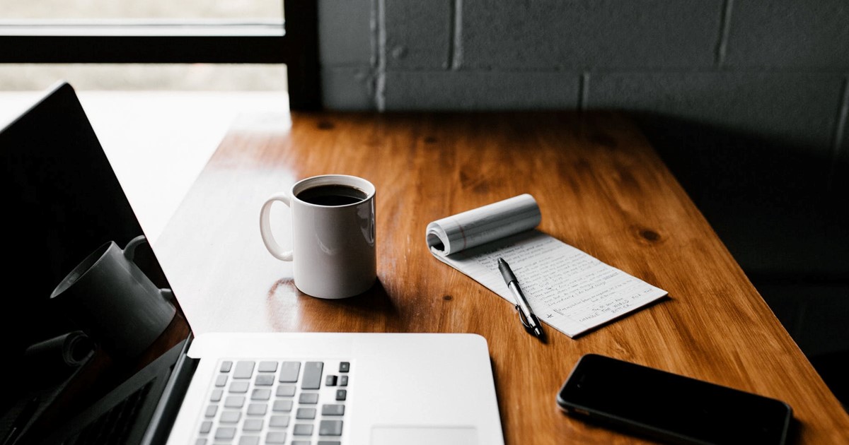 Desk with laptop, coffee, notepad and mobile phone