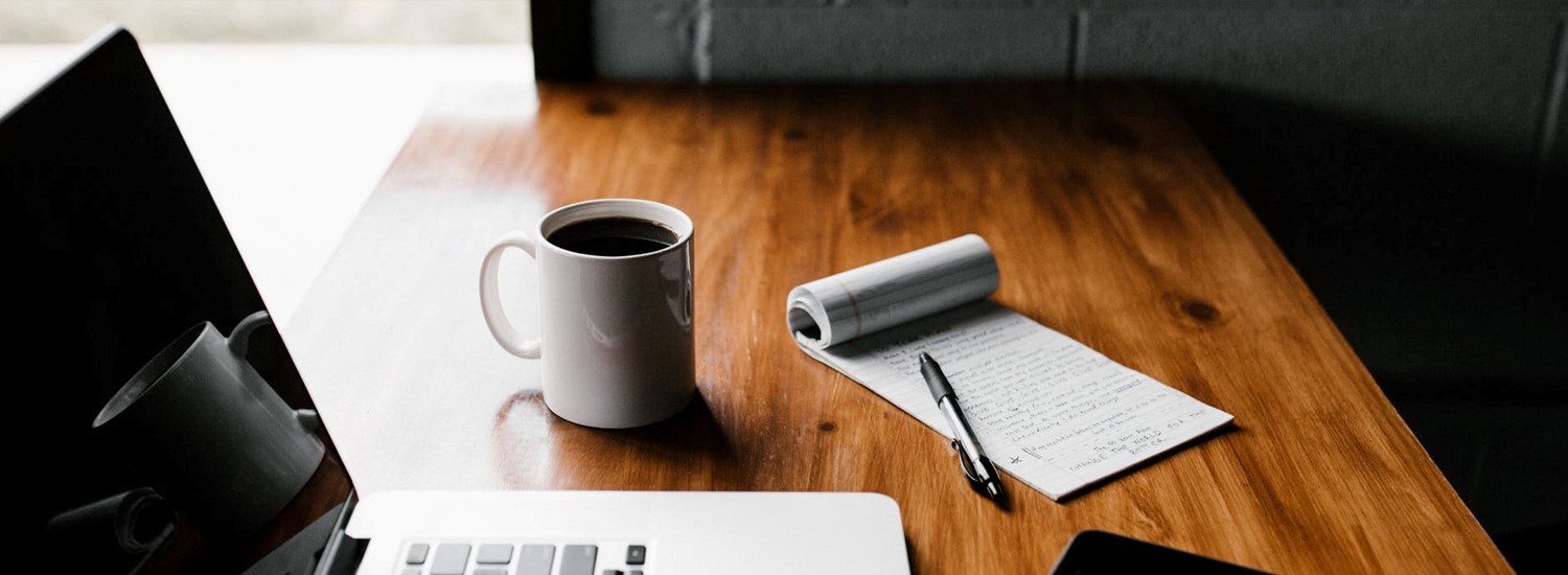 A laptop, mug, pad, paper and mobile phone on a desk