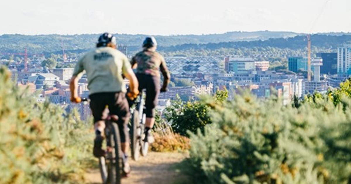 Two cyclists on track through park with city in the foreground