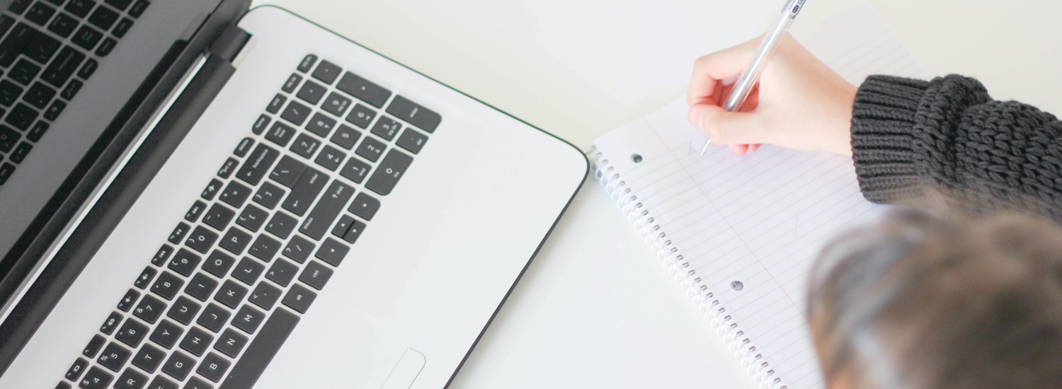 Stock image of a woman writing on a notepad in front of a laptop