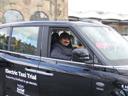 Taxi driver smiling behind the wheel of a black electric taxi 