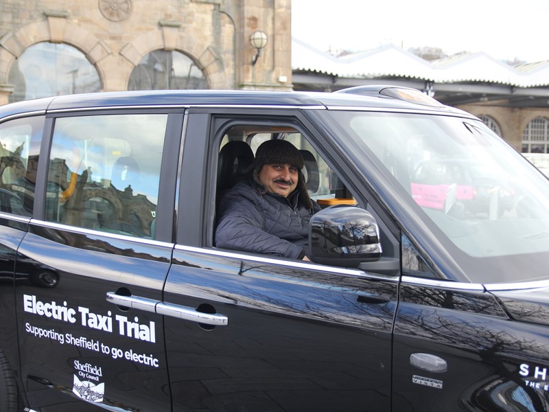 Taxi driver smiling behind the wheel of a black electric taxi 