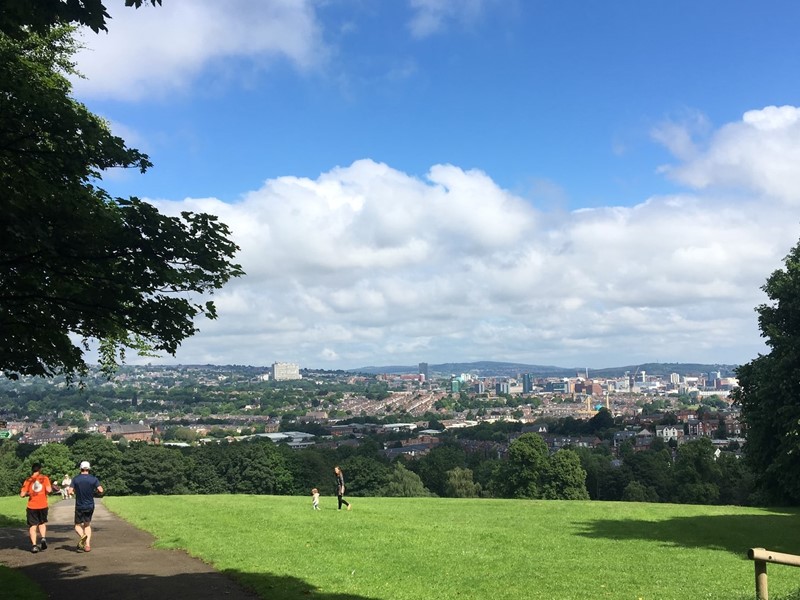 Blue skies over a Sheffield park with people running and walking through it