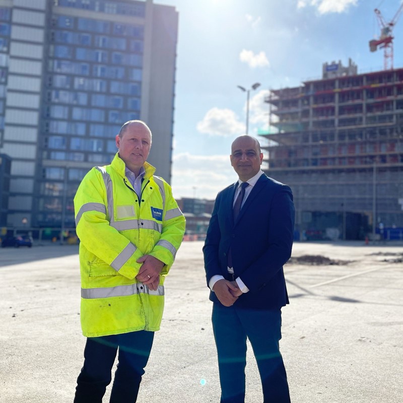 Two men stood on construction site, one in high vis, one in a suit.