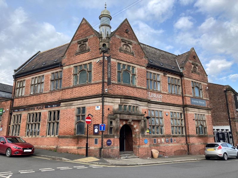 Attercliffe Library building underneath a blue sky dotted with white clouds, to the far right of the building is a silver car parked on the roadside and to the far left is a red car parked by the roadside