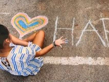 Child in striped dress sitting in a playground chalk drawing on the concrete 'I heart hap'