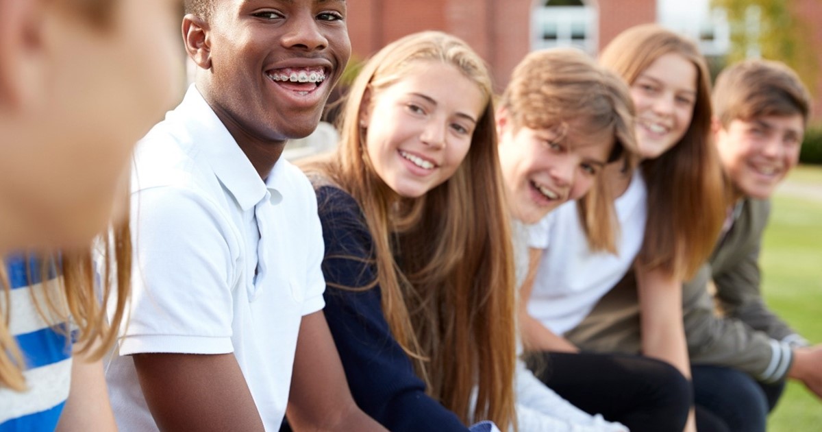 Young people sitting in a row, 4 white people and a black person with braces