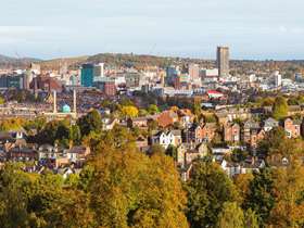 A panoramic view of Sheffield with trees lining a park, rows of houses and the city skyline in the distance
