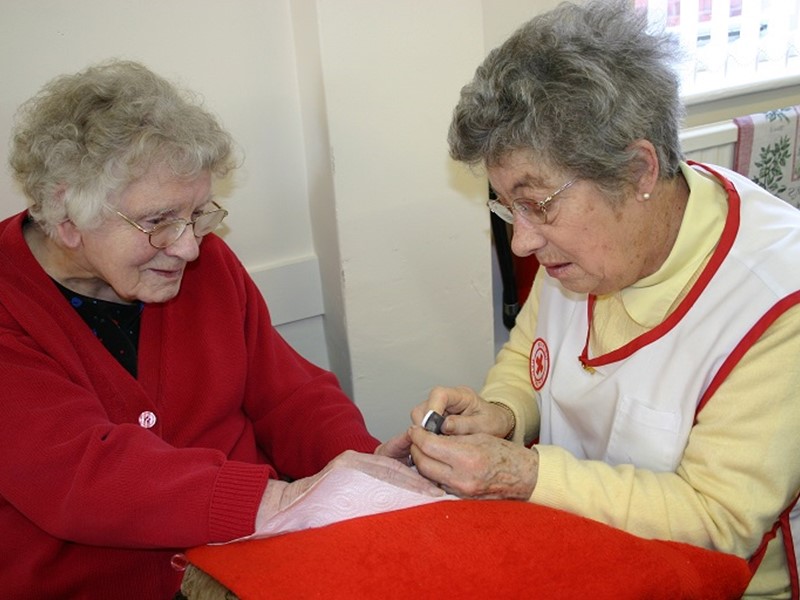 Woman in red cardigan sitting at table having her nails cared for by another woman
